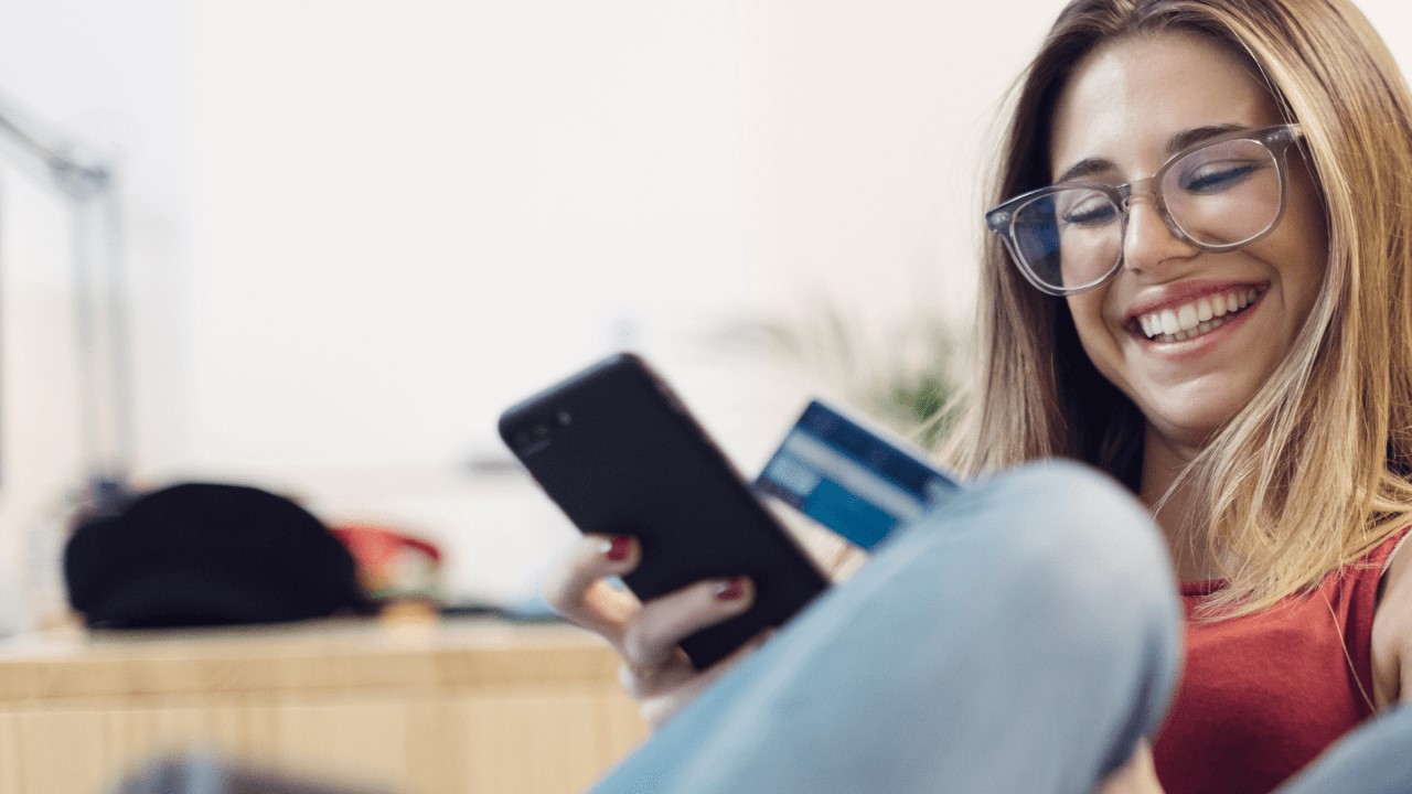 Ung kvinne med briller smiler og ser på mobilen